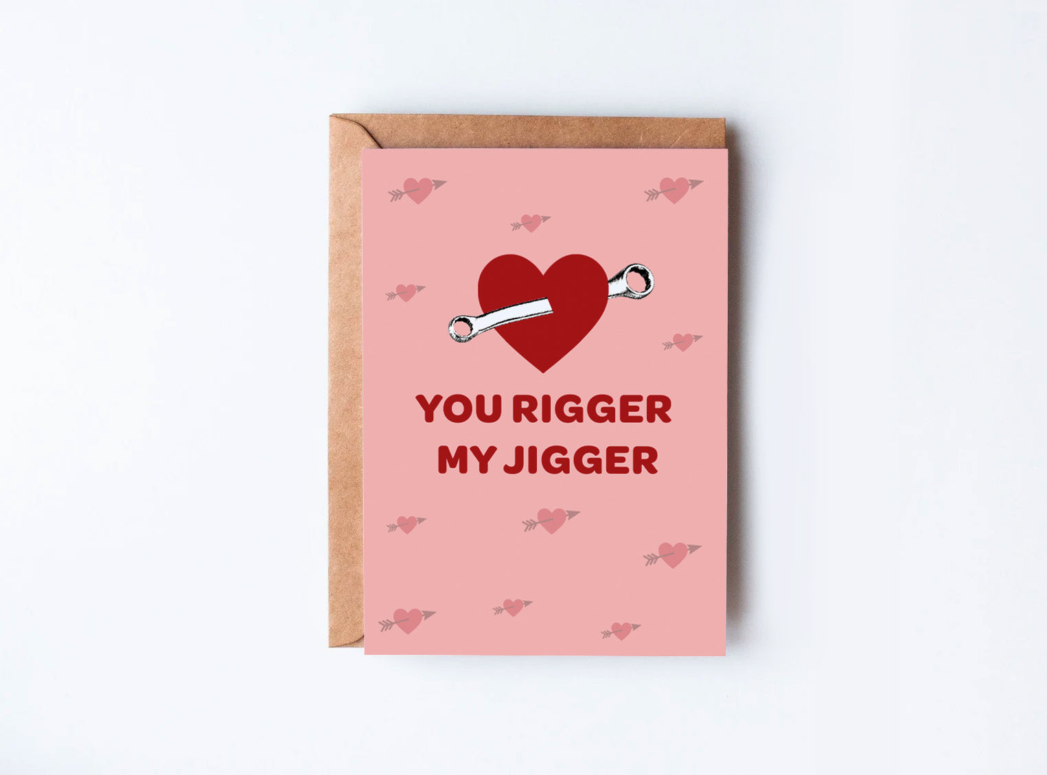 Rowing Card with a pink background and a red heart with a rigger jigger piercing it, with the words 'you rigger my jigger' printed below the graphic